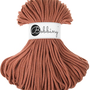 May include: A large spool of terracotta colored cotton cord, labeled "Bobbiny" in black lettering.