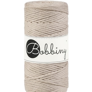 May include: A beige spool of cotton cord with the brand name "Bobbiny" printed on a white label.