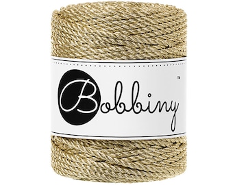 May include: A spool of gold metallic rope with a white label that says "Bobbiny" in black cursive lettering.
