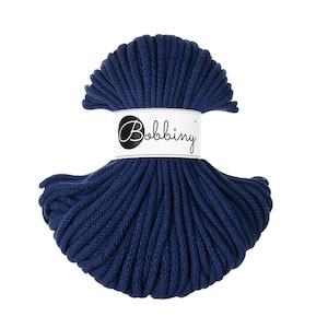 Op de afbeelding: Een bol marineblauw macramé koord. Het koord is strak opgerold en omwikkeld met een wit label met de tekst "Bobbiny". Het koord heeft een diepe, verzadigde blauwe kleur. Perfect voor knutselprojecten.