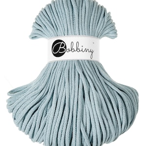 Puede incluir: Un ovillo de cuerda de algod&oacute;n azul claro, tambi&eacute;n conocida como cuerda, cord&oacute;n o hilo. La cuerda est&aacute; enrollada en forma circular y tiene una etiqueta que dice "Bobbiny".
