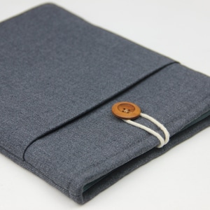 May include: A gray fabric book cover with a wooden button closure. The cover is made of a textured material and has a simple design.