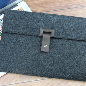 Op de afbeelding: Een grijze laptophuls van vilt met een bruine leren flap en een drukknoop.