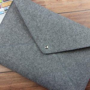 May include: Gray felt laptop sleeve with a flap closure and a silver button. The sleeve is lying on a wooden surface.