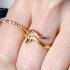May include: A gold snake ring with a textured band. The ring is worn on a finger with a second gold band ring.