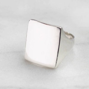 May include: A silver signet ring with a square top. The ring is smooth and polished.