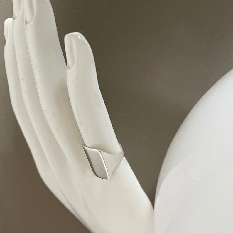 May include: A silver signet ring with a flat, rectangular top.
