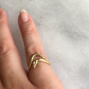 May include: A gold snake ring with green eyes. The snake is wrapped around the finger.