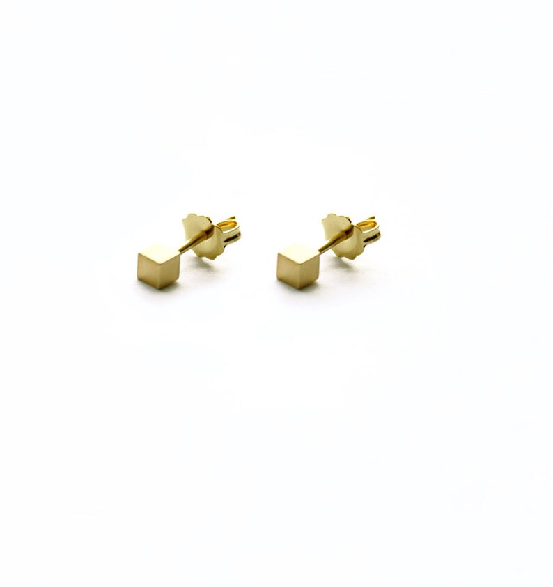 Op de afbeelding: Een paar gouden kubus oorbelletjes. De oorbelletjes zijn klein en simpel, met een minimalistisch ontwerp.