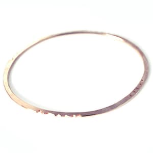 Pode incluir: Um bracelete fino de ouro rosa com uma borda texturizada e uma fileira de pequenos pontos ao longo da parte inferior.