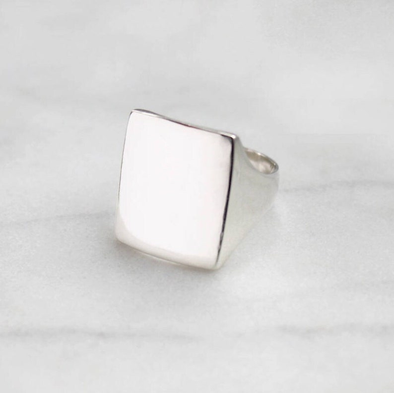 May include: A silver signet ring with a square top. The ring is smooth and polished.