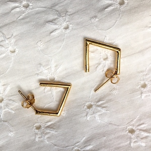 May include: A pair of gold-toned geometric hoop earrings. The earrings are made of a thick, square-shaped wire.