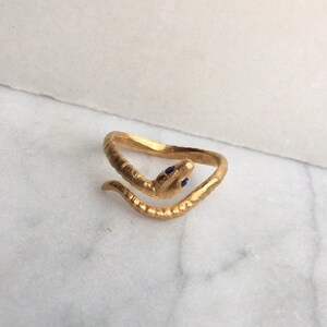 May include: A gold snake ring with blue sapphire eyes. The ring is textured and has a coiled snake design.