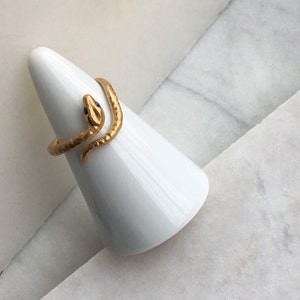 May include: A gold snake ring with blue eyes, displayed on a white cone-shaped ring holder.