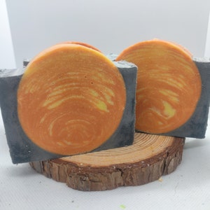 May include: Two bars of handmade soap with a swirl design. The soap is a combination of gray and orange.