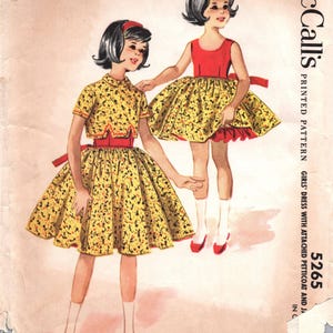 May include: Vintage McCall's printed pattern for girls' dresses. The illustration shows two girls in dresses with yellow skirts and red accents. The dresses have a floral pattern. The text on the pattern reads "McCall's" and "5265".