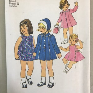 May include: Simplicity sewing pattern number 7323 for a toddler dress. The pattern includes three different dress styles: a blue dress with a white collar and a white hat, a pink dress with a white collar, and a floral print dress with a white collar. The pattern is for size 4, with a 23-inch breast measurement.