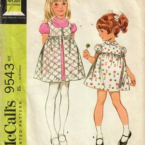 May include: Vintage McCall's sewing pattern for a child's dress and jumper. The illustration shows two young girls wearing dresses. One dress is pink and white with a floral pattern, and the other is white with a pink and white pattern. The pattern number is 9543.