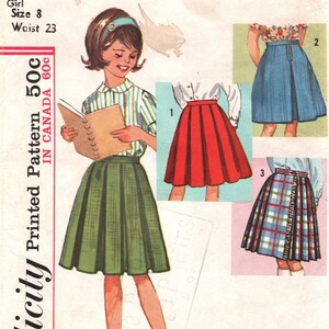Puede incluir: Sobre de patrón Simplicity vintage con una niña con falda plisada verde, camisa a rayas y diadema. El sobre incluye ilustraciones de diferentes estilos de faldas. El texto en el sobre dice "Girl Size 8 Waist 23".