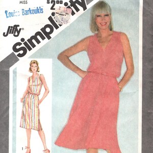 Op de afbeelding: Simplicity patroonhoes met een vrouw in een koraalkleurige jurk. De hoes bevat nummer 9895, maat 14 en de tekst "Jiffy". De jurk heeft een V-hals en een midi-rok.