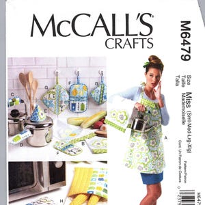 May include: A McCall's Crafts sewing pattern package, M6479, featuring a woman wearing an apron. The image includes various kitchen accessories like pot holders, oven mitts, and a pot. The package also shows body measurements in inches.