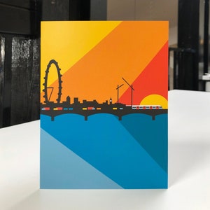May include: A colorful art print featuring a London skyline silhouette against a gradient sunset. The design includes the London Eye, buildings, a bridge, and a train, with a blue and yellow background.
