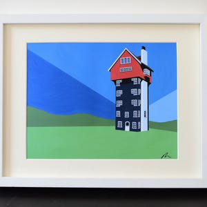 May include: Framed art print depicting a tall, stylised building with a red roof and white chimney. The building is mainly dark blue with white windows, set against a blue sky and green field. The artwork is in a white frame.