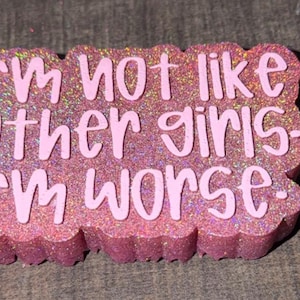 May include: A rectangular pink glittery plaque with scalloped edges featuring the raised white text "I'm not like other girls. I'm worse." The surface has a dense, sparkling texture that reflects light, and the lettering is in a clean, sans-serif font.