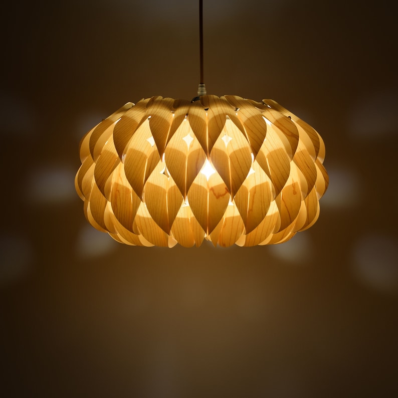 May include: A wooden pendant light fixture with a unique, geometric design. The light is made up of many small, overlapping pieces of wood that create a honeycomb-like pattern. The light is illuminated, casting a warm glow.