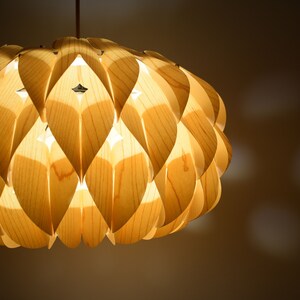 May include: A light wood pendant lamp with a unique design featuring overlapping, petal-like shapes. The lamp is illuminated, casting a warm glow.