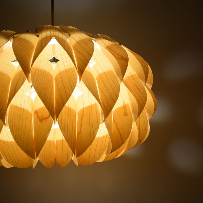 May include: A light wood pendant lamp with a unique design featuring overlapping, petal-like shapes. The lamp is illuminated, casting a warm glow.