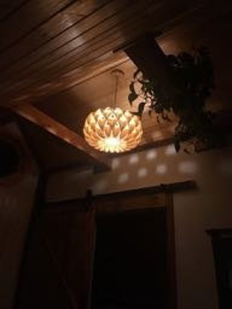 May include: A wooden pendant light fixture with a unique, geometric design. The light is hanging from a ceiling with wood paneling and casts a warm glow.