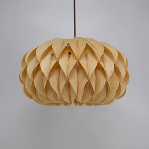 May include: A light wood pendant lamp with a unique design featuring overlapping, curved wooden pieces that resemble petals. The lampshade is round and has a natural wood finish.