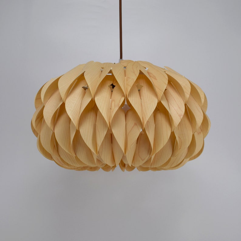 May include: A light wood pendant lamp with a unique design featuring overlapping, curved wooden pieces that resemble petals. The lampshade is round and has a natural wood finish.