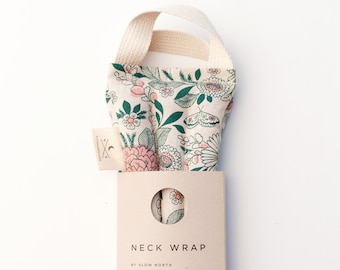 May include: A floral neck wrap with a cream-colored handle and a cream-colored background. The wrap features a botanical pattern with pink flowers, green leaves, and butterflies. The product is packaged with a brown paper label that reads "NECK WRAP".