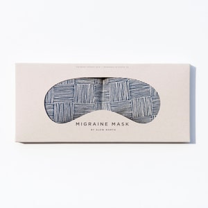 May include: A white box with a blue and white striped eye mask inside. The box says "Migraine Mask by Slow North".
