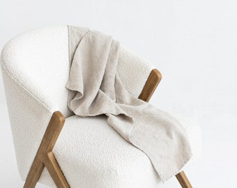 May include: A white armchair with a light brown wooden frame and a beige throw blanket draped over the seat.