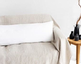 May include: A white linen sofa with a white throw pillow and a wooden side table with black decorative bottles and a dried branch. A black teapot and two cups are on a wooden tray on the floor.