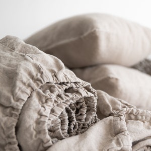 May include: A close-up of a beige linen fitted sheet, rolled up and ready to be placed on a bed. The sheet is made of natural linen fabric, known for its breathability and durability.