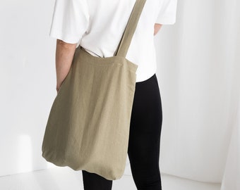 May include: A person wearing a white t-shirt and black pants is carrying a large, olive green tote bag over their shoulder.