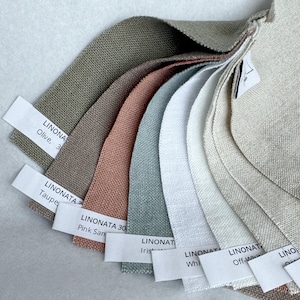 May include: A fan-shaped collection of fabric swatches in various colors including olive, taupe, pink sand, iris, white, and off-white. Each swatch features a white paper label with the text LINONATA and the specific color name printed in black.