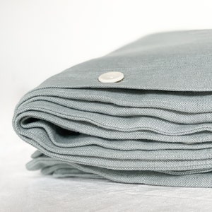 K&ouml;nnte beinhalten: Ein gefalteter, hellblauer Leinen-Bettbezug mit einem wei&szlig;en Knopfverschluss.