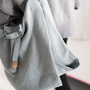 May include: A light blue linen tote bag with a brown leather strap. The bag is folded over and has a simple design.