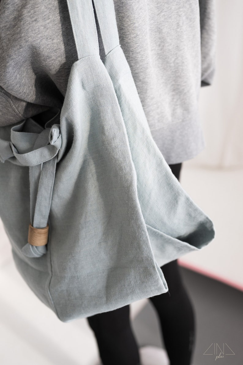 May include: A light blue linen tote bag with a brown leather strap. The bag is folded over and has a simple design.