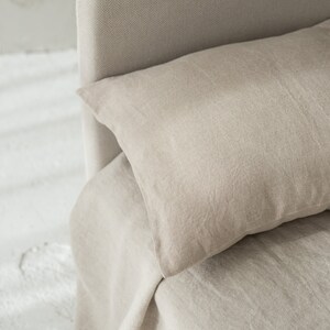 May include: A close-up of a beige linen bed with a pillow. The bed is made with a soft, natural fabric and has a simple, elegant design.