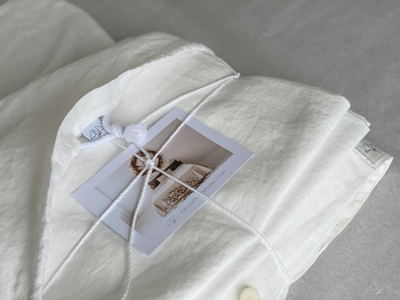 Puede incluir: Un juego de funda n&oacute;rdica de lino blanco atado con cuerda y una tarjeta blanca con el texto "FOR COVER 150x200 cm - 100% LINEN" en ella.