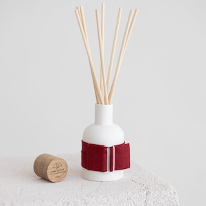 May include: White ceramic diffuser bottle with a red fabric band and wooden sticks. The bottle has a wooden cap with the text "HOME SCENTS" and "JOY" printed on it.