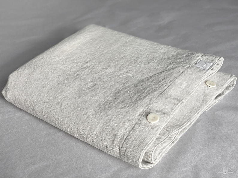 May include: A gray cotton duvet cover with two white buttons. The duvet cover is folded and has a textured surface.