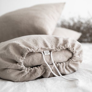 May include: A beige linen pillowcase with a drawstring closure and a white label with the text "Linen & Love" on it.