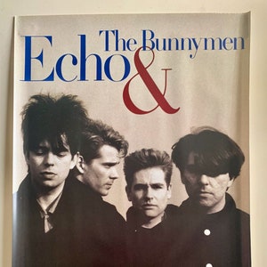 May include: A black and white promotional poster for the band The Bunnymen. The poster features a photo of the band members, with the band's name and the album title "Echo & The Bunnymen" in large, bold letters.
